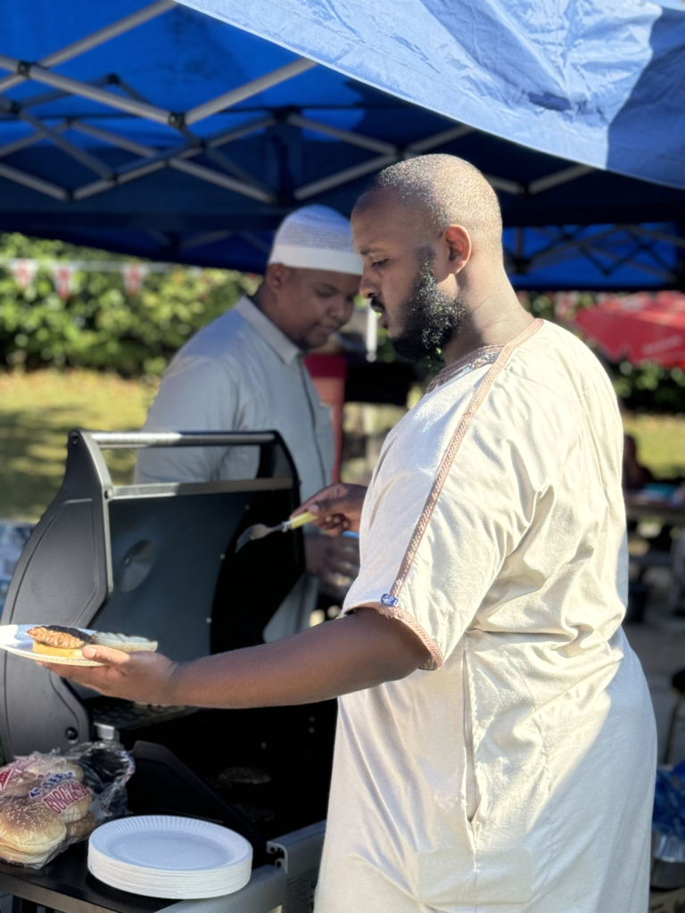 A-man-wearing-a-traditional-light-colored-thobe-holds-a-plate-with-a-freshly-grilled-burger_-standin