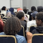 A view from behind the crowd showing members of the audience seated during the presentation_jfif