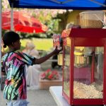 A young boy getting popcorn from a red popcorn machine set up under a blue canopy tent_jfif