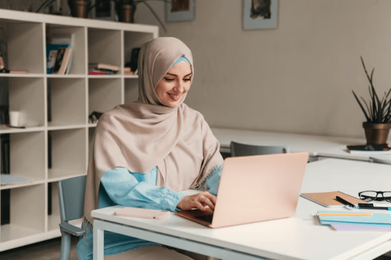 A young woman Working on a laptop, with a smartphone, notebook, pen, and glasses nearby on the desk_png