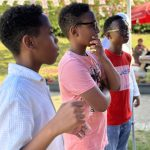 Three young boys standing side-by-side watching an outdoor game or activity with focused expressions_jfif