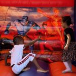Two children playing and jumping inside a colorful, superhero-themed inflatable bouncy house_jfif